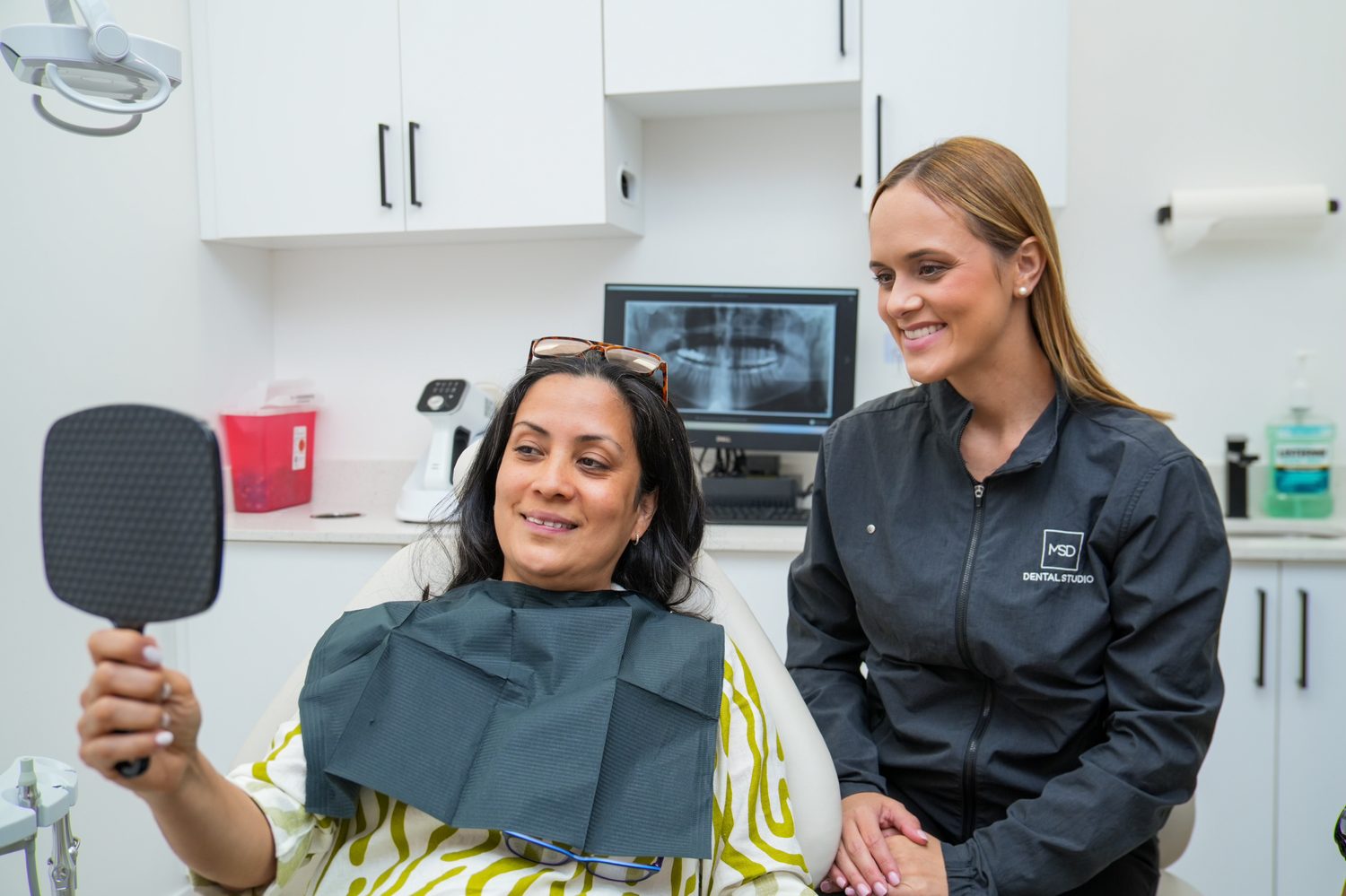 Una paciente viendo su nueva sonrisa en el espejo con su clínica en MSD Dental Studio, Coral Springs